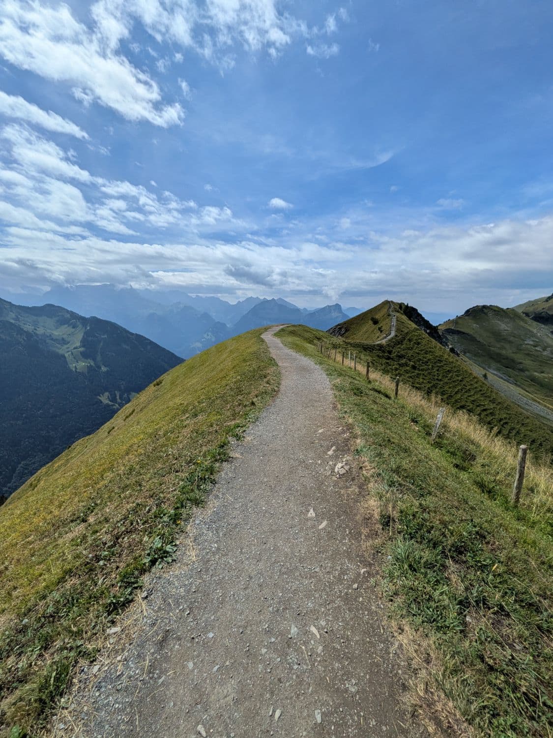 A gravel trail along a green mountain ridge in the Swiss Alps
